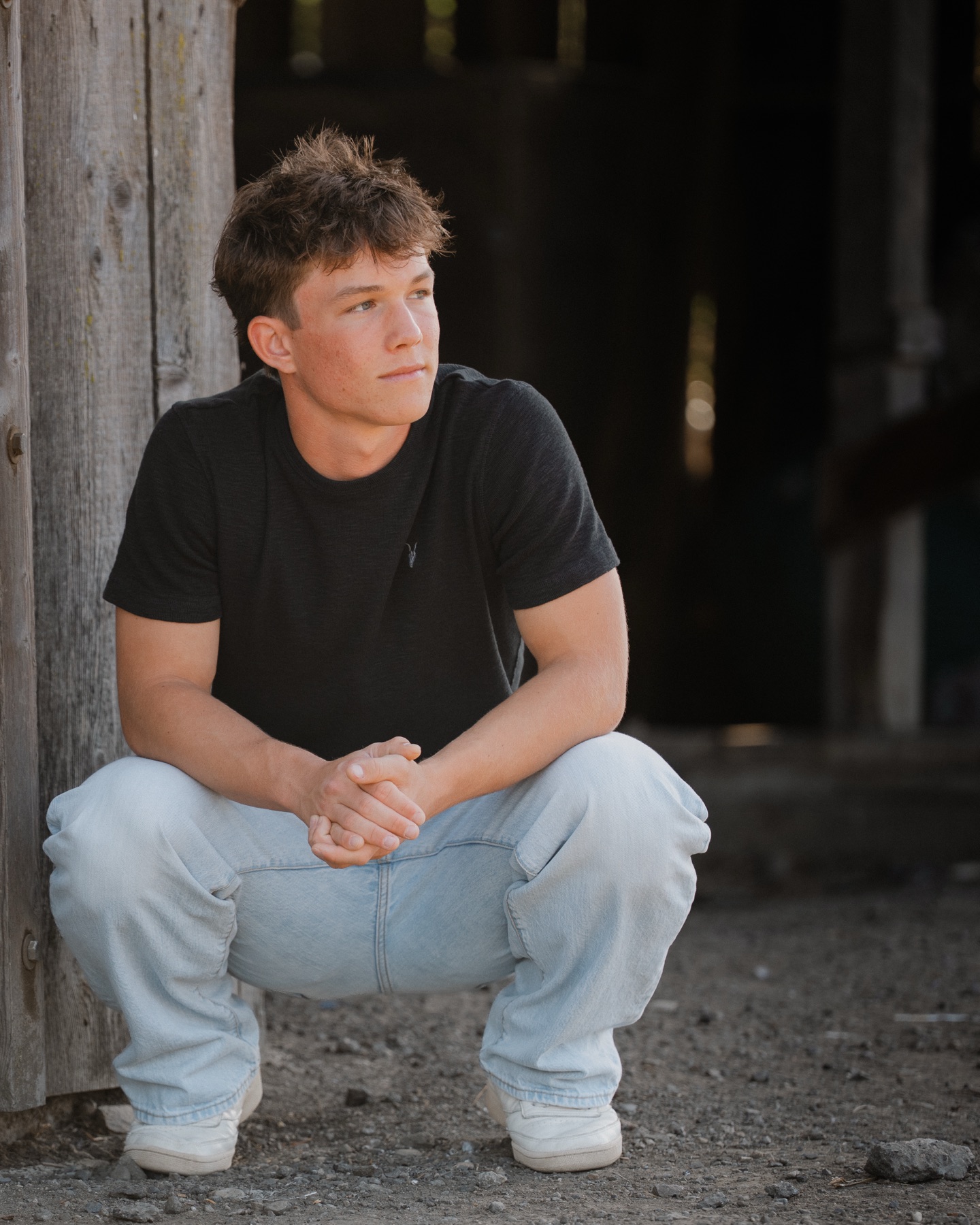 Senior crouching beside a weathered barn wall, looking off camera — Central Coast senior photographer