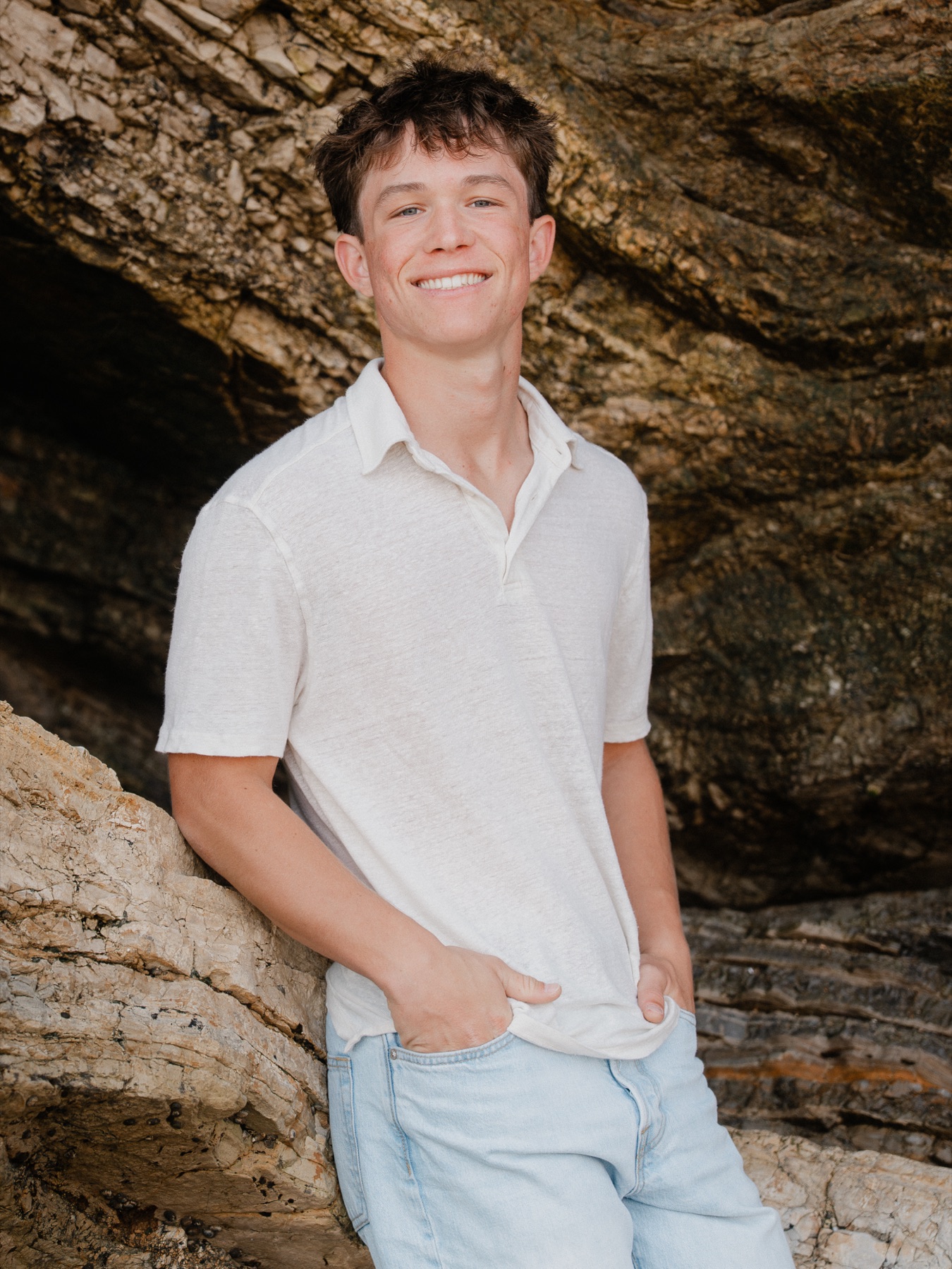 Senior smiling, leaning on coastal rocks beside a sea cave — Central Coast senior photographer