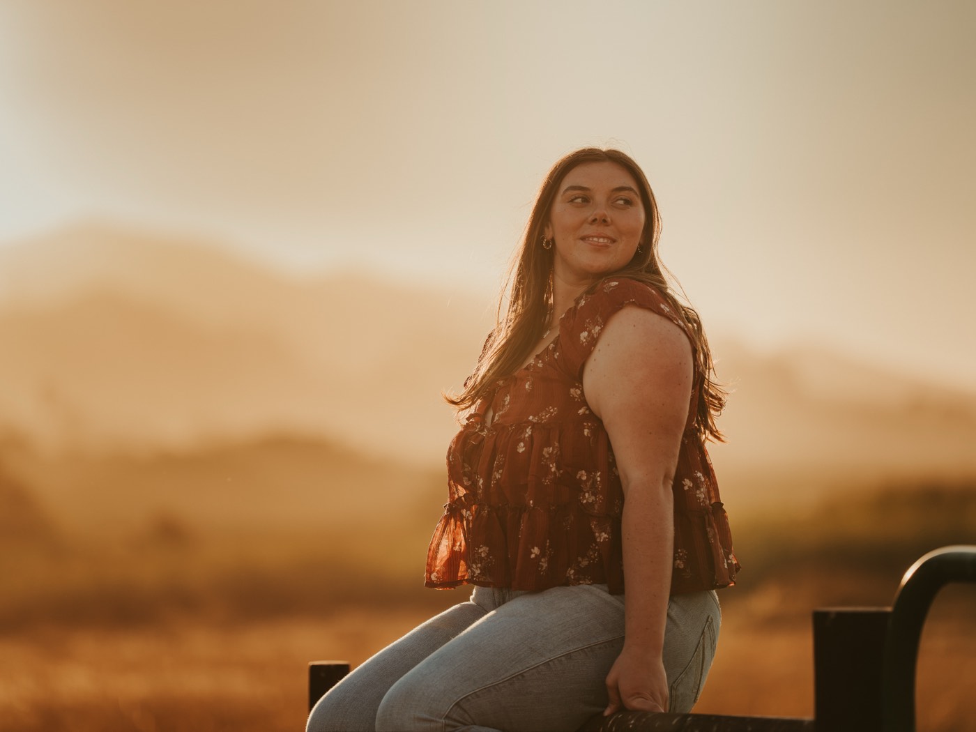 Senior portrait backlit at golden hour, sitting on a fence line — Central Coast senior photographer