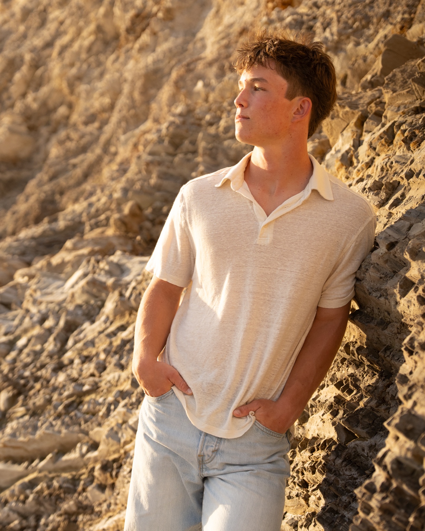 Senior leaning against golden coastal cliffs at sunset, hands in pockets — Central Coast senior photographer