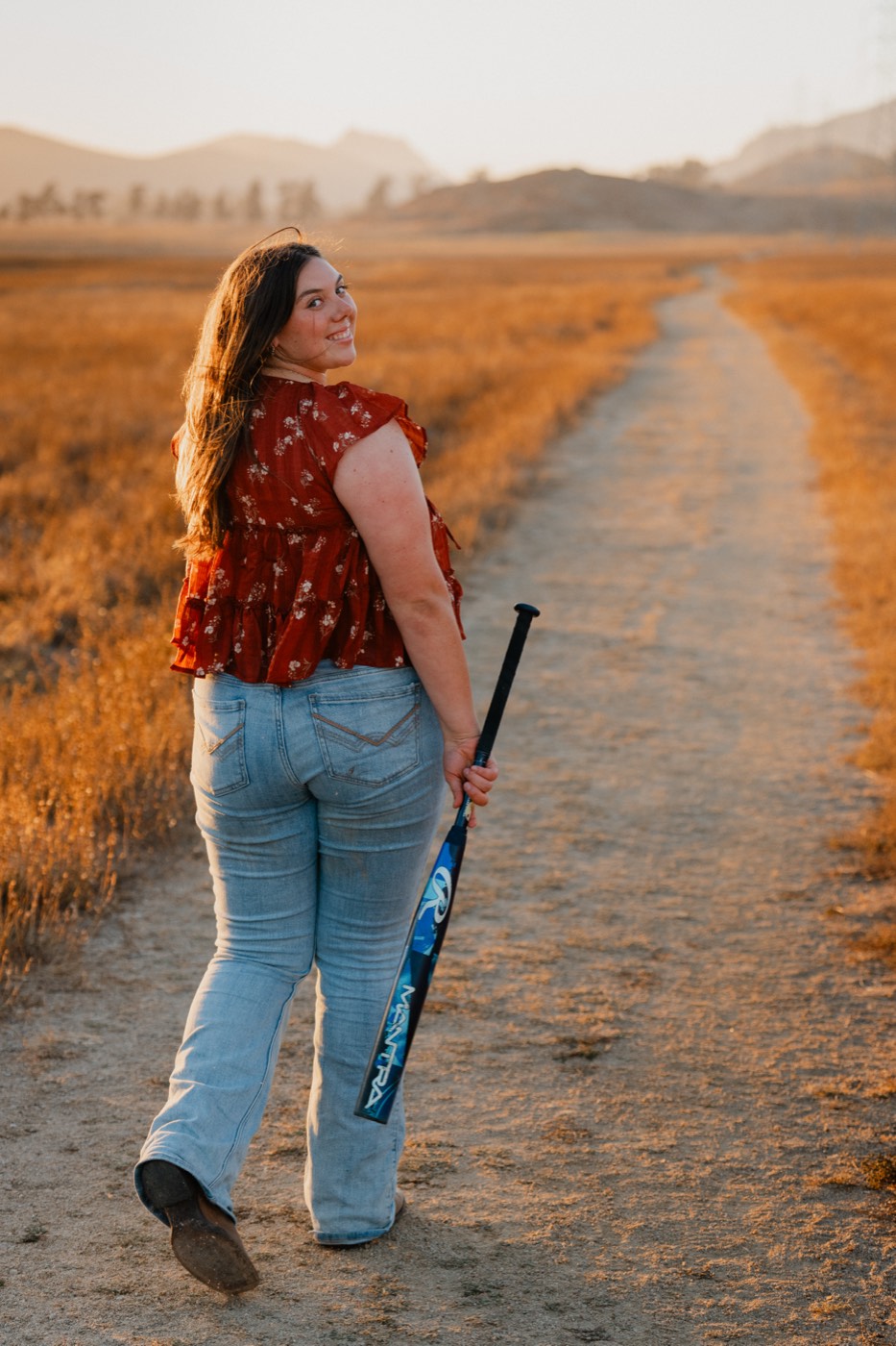 Senior softball player walking a golden hour field path, bat in hand — Central Coast senior photographer