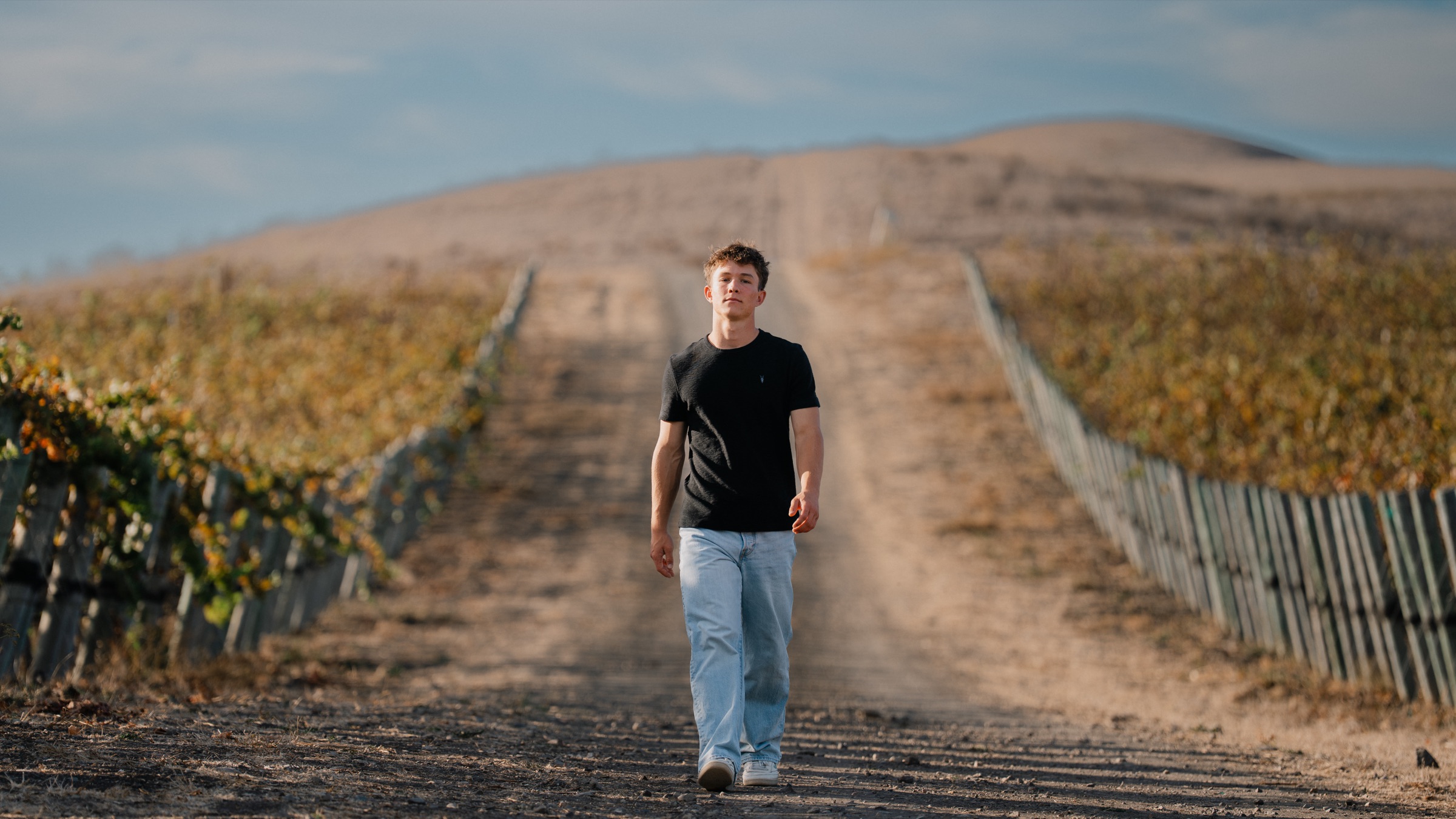 Senior boy walking down a vineyard dirt road at golden hour, Central Coast California